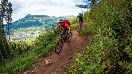 Hahnenkamm Trail © TVB Kitzbüheler Alpen-Brixental, Fotograf Andreas Meyer Two mountain bikers riding on a narrow mountain trail overlooking a valley