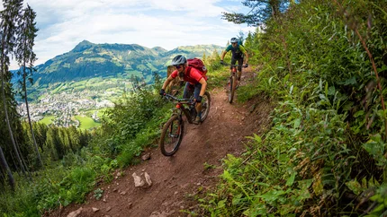 Hahnenkamm Trail © TVB Kitzbüheler Alpen-Brixental, Fotograf Andreas Meyer Two mountain bikers riding on a narrow mountain trail overlooking a valley