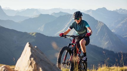 Bregenzerwald © Bregenzerwald Tourismus - Sebastian Stiphout Woman mountain biking in the mountains on a sunny day wearing helmet and sunglasses