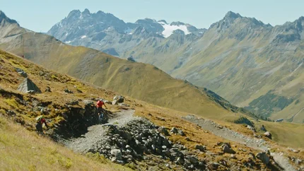 HOCHPAZNAUN © David Karg Mountain bikers on rocky trail in Alps with snow-capped peaks in background