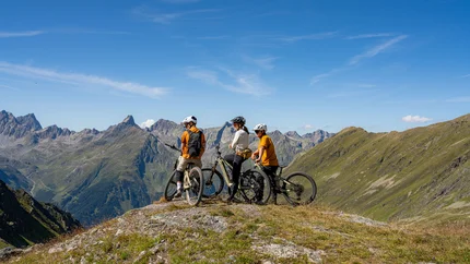 Höllkar Trail © Markus Greber Three cyclists with helmets on a mountain overlooking alpine peaks