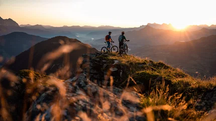 BRECHHORN © TVB Kitzbüheler Alpen Brixental - Mathäus Gartner Two mountain bikers on a summit watching the sunset