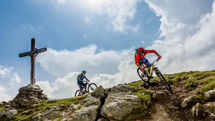 Herrnsteig Trail © Kirsten Sörries Two mountain bikers riding rocky mountain trail near a wooden cross