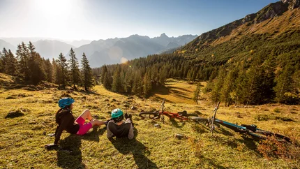 MTB Tour from Brand to Bürs © Michael Marte Two cyclists wearing helmets resting on mountain meadow overlooking forested valleys