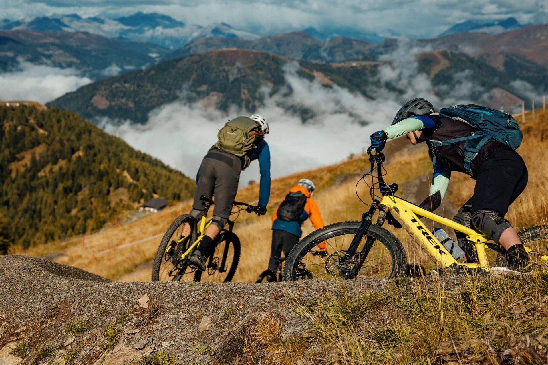 Mountain Bike Holidays © David Karg Drei Mountainbiker fahren auf einem Pfad in den Bergen bei klarem Himmel