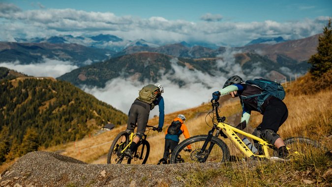 Mountain Bike Holidays © David Karg Drei Mountainbiker fahren auf einem Pfad in den Bergen bei klarem Himmel