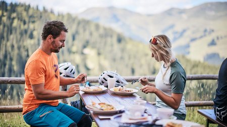 Bike & Cuisine © Tobias Köhler Two people eating outdoors with a mountain landscape behind them