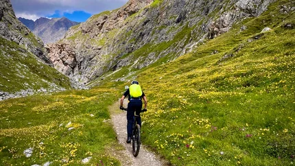 VAL D'UINIA - THREE-COUNTRY TOUR © Hanna Putz Cyclist with green backpack on mountain trail between rocks and flowers