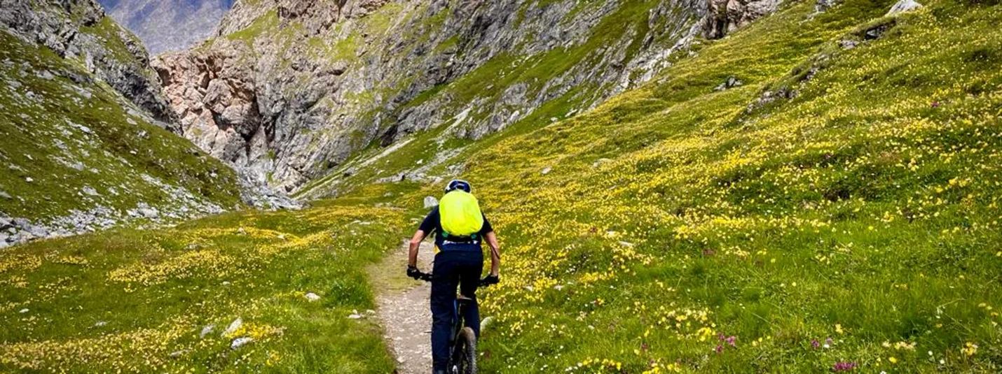 VAL D'UINIA - THREE-COUNTRY TOUR © Hanna Putz Cyclist with green backpack on mountain trail between rocks and flowers