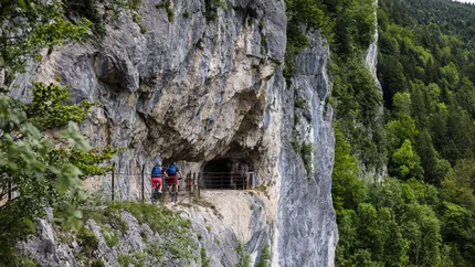 BergeSeen eTrail © Norman Bielig Two cyclists on narrow mountain path near rock cave and forest