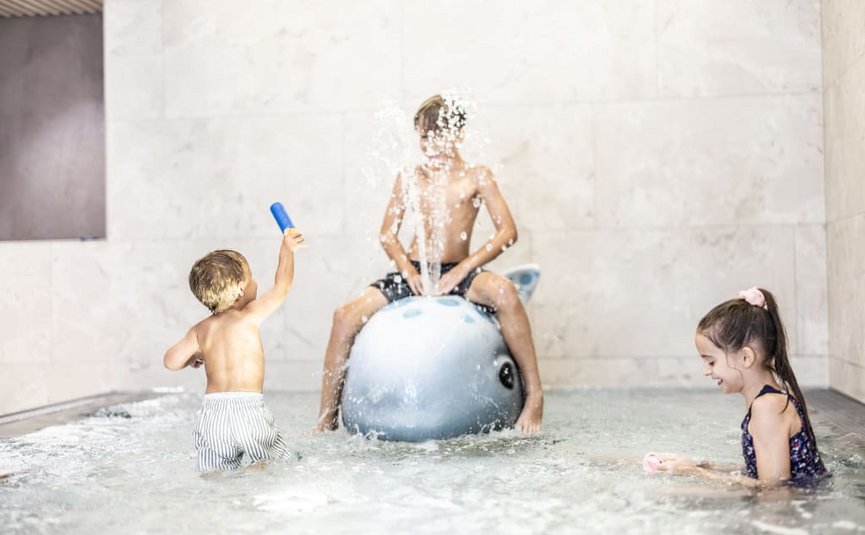 Familienurlaubswoche Kinder spielen im Schwimmbad mit Wasserspielzeug und spritzendem Wasser