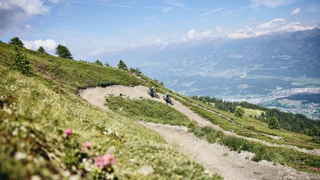 Quality Promise © Tobias Köhler Two mountain bikers on winding trail with alpine mountain views