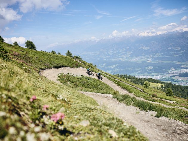 Quality Promise © Tobias Köhler Two mountain bikers on winding trail with alpine mountain views