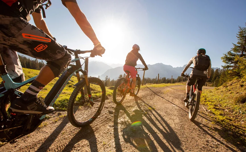 Mountain bike holiday in Brandnertal © Michael Marte - Bikepark Brandnertal Three mountain bikers riding on sunny mountain trail with mountains behind