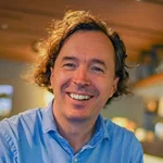 Mountain Bike Holidays © Hotel Walliserhof Mann in blauem Hemd lächelt in einem gemütlichen Café