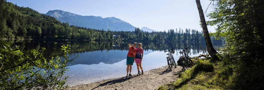 Mountain bike holidays in Styria © Velontour Two cyclists taking a selfie by the lake with mountains in the background