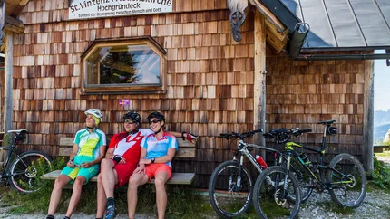 Hochgründeck Tour © Salzburger Sportwelt - Coen Weesjes Three cyclists sitting on a bench in front of St. Vinzenz Peace Church