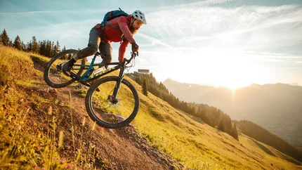 STEINBERGKOGEL VIA HAHNENKAMM © David Karg Mountain biker riding downhill at sunset on a mountain trail