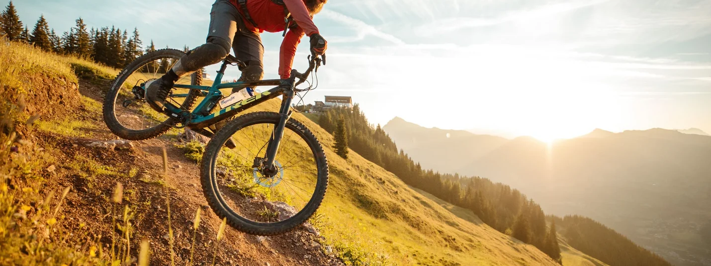 STEINBERGKOGEL VIA HAHNENKAMM © David Karg Mountain biker riding downhill at sunset on a mountain trail