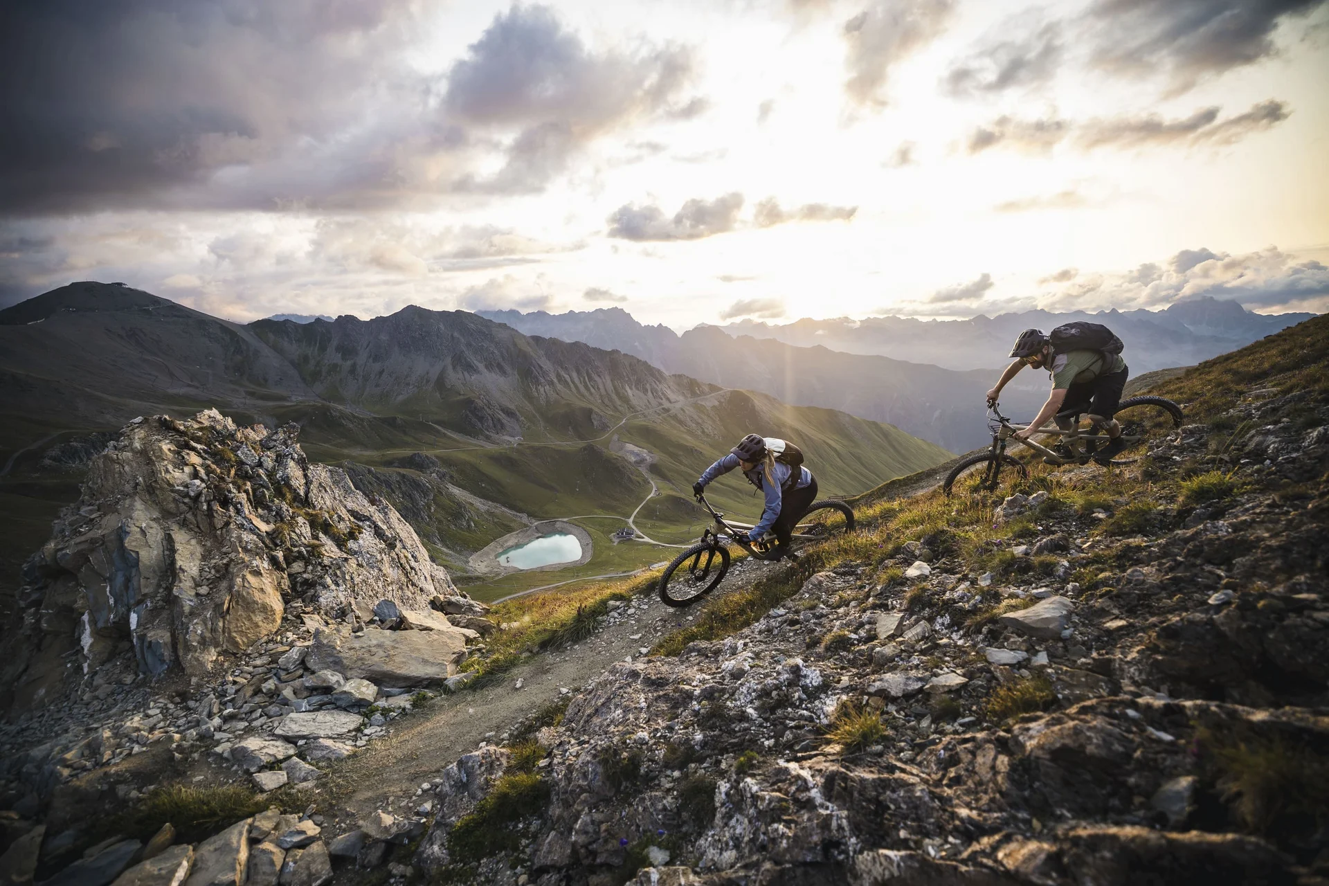 Mountain Bike Holidays © TVB Paznaun – Ischgl Zwei Mountainbiker fahren auf einem steilen Bergpfad mit Bergpanorama