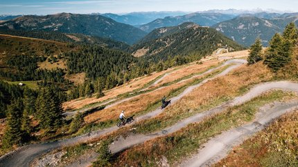 NOCKBIKE region © Jens Scheibe Two cyclists on a winding mountain trail surrounded by forests and mountains