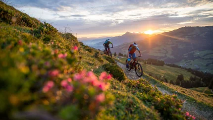 WIEGALM © TVB Kitzbüheler Alpen Brixental - Andreas Meyer Two mountain bikers riding on a mountain trail at sunset