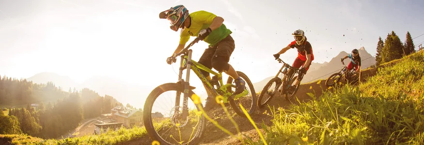 Brandnertal © Michael Marte - Bikepark Brandnertal Three mountain bikers riding downhill on a sunny forest trail