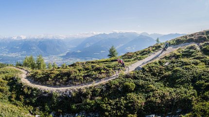 San Vigilio Dolomites - Kronplatz © Harald Wisthaler Mountain bikers riding on a mountain trail with alpine landscape under sunny sky