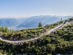 San Vigilio Dolomites - Kronplatz © Harald Wisthaler Mountain bikers riding on a mountain trail with alpine landscape under sunny sky