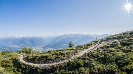 Herrnsteig - The legend © Harald Wisthaler Mountain bikers riding on a mountain trail with alpine landscape under sunny sky