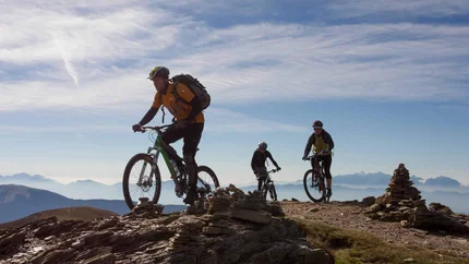 Alpe Adria World War Transalp © Hotel Lindenhof Three mountain bikers riding on a rocky mountain trail under a clear sky