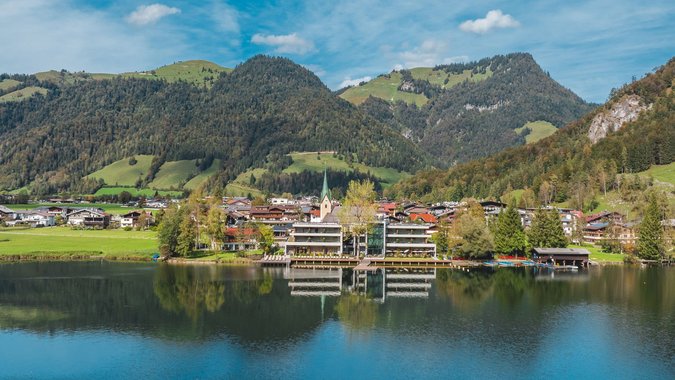 Mountain Bike Holidays © Mathhäus Gartner Bergdorf am See mit bewaldeten Hügeln und blauen Himmel im Hintergrund