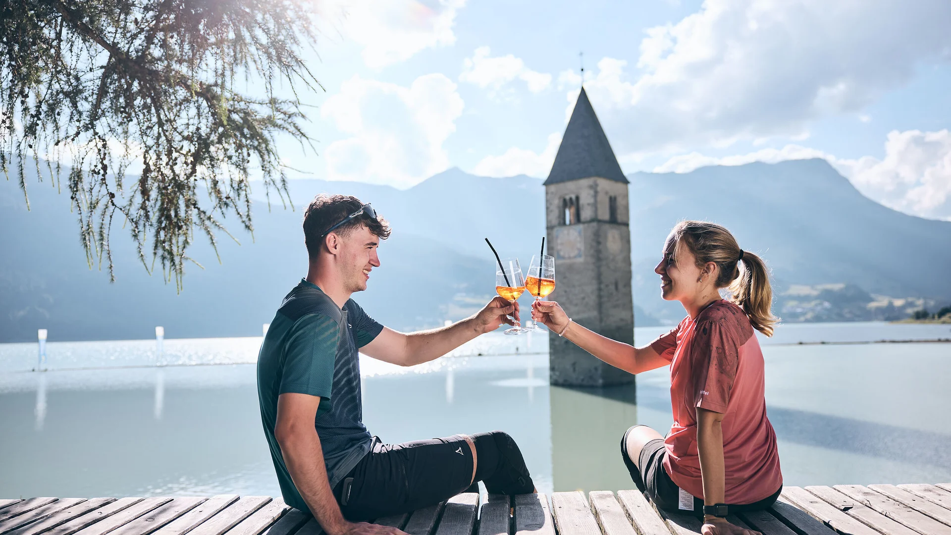 Mountain Bike Holidays © Tobias Köhler Junges Paar stößt mit Aperol am gefluteten Kirchturm in Reschen an.