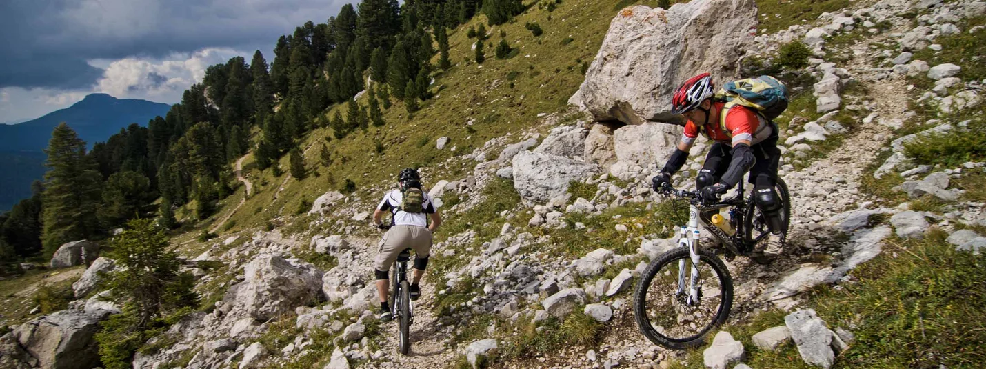 LATEMAR OMZEILING © Exploring GmbH Twee mountainbikers op een rotsachtig bergpad met groene bomen