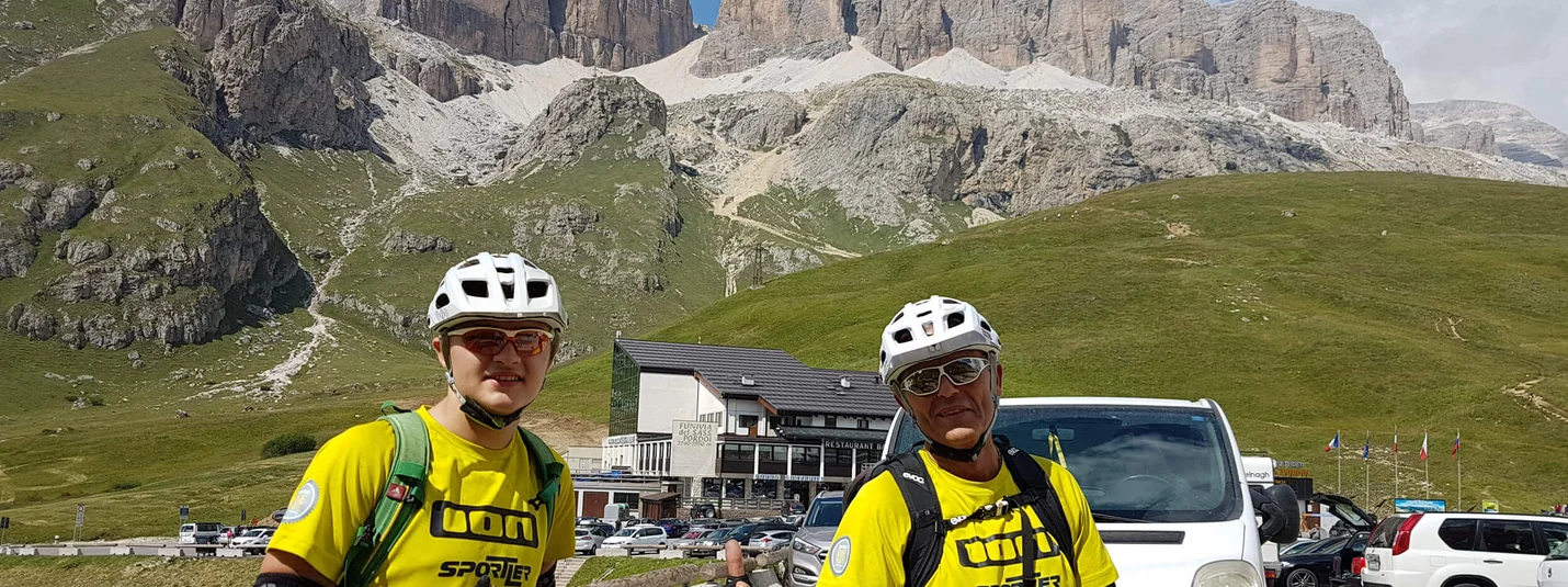 Anratterhütte © Hotel Jonathan Two cyclists in yellow jerseys with mountain and parked cars behind