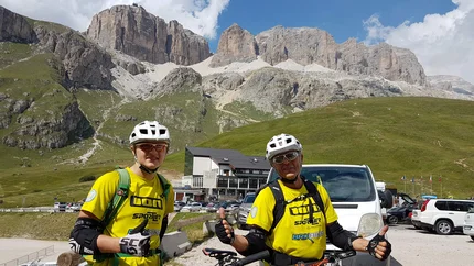 Anratterhütte © Hotel Jonathan Two cyclists in yellow jerseys with mountain and parked cars behind