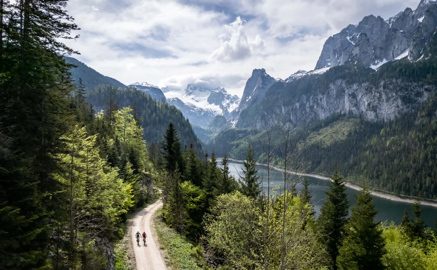 Mountain bike holiday in the Salzkammergut © Bikeboard.at - Erwin Haiden Two cyclists on forest trail by lake with snowy mountain peaks