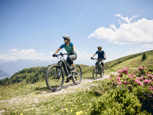 Quality Promise © Tobias Köhler Two people riding e-mountain bikes on a mountain trail on a sunny day