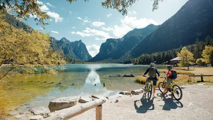 Marchkinkele © David Karg Two cyclists by a lake with mountains on a sunny day