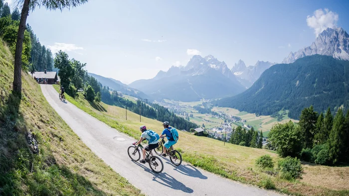 Multi-day tours © www.wisthaler.com Two cyclists on mountain road overlooking valley and mountains in sunlight