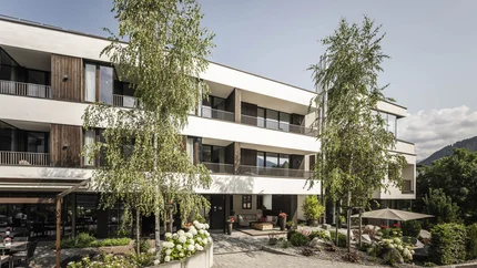 Alpinhotel Keil © Hannes Niederkofler Modernes dreistöckiges Gebäude mit Bäumen und Sitzbereichen im Hof