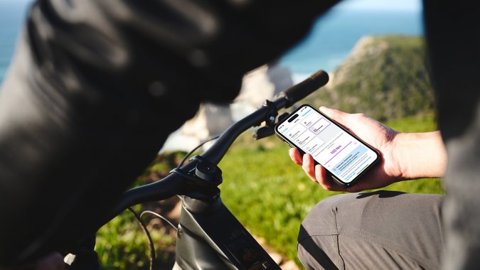 Mountain Bike Holidays © Bosch eBike Systeme Person hält Smartphone mit Fahrrad-App neben Fahrradlenker im Freien