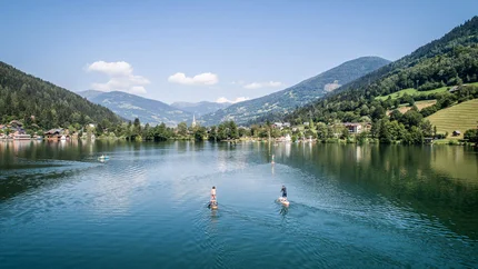 Karinthië rijk aan water © Gert Perauer Mensen op paddleboards op een meer met bergen en dorpen op de achtergrond