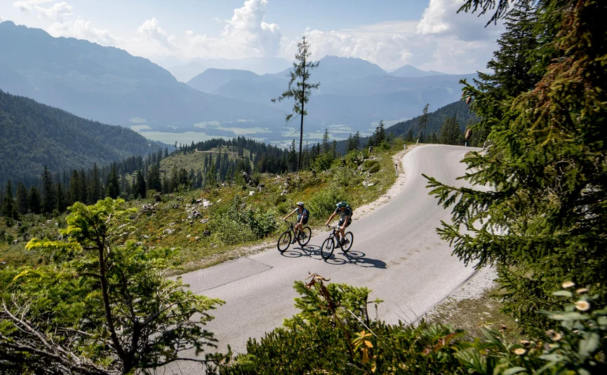 Mountain bike holidays in Styria © TVB Ausseerland Salzkammergut - Tom Lamm Two cyclists riding on mountain road with forest and mountains in background