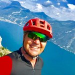 Mountain Bike Holidays © Andrea Maino Mann mit rotem Fahrradhelm vor Berg und See in sonniger Landschaft