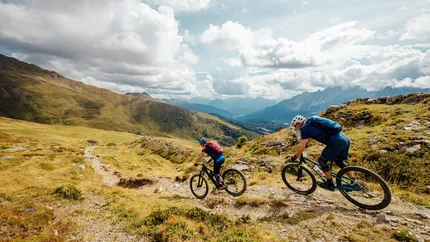 South Tyrol © David Karg Two mountain bikers riding on a rocky mountain trail under cloudy sky