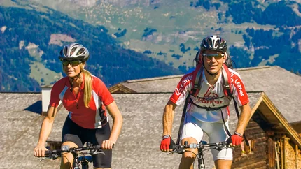 Moosalm - Eben MTB Tour © Hotel Montanara Man and woman mountain biking on green field with mountains in background