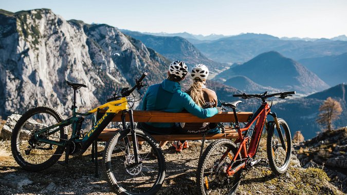 Mountain Bike Holidays © TVB Ausseerland Salzkammergut - Katrin Kerschbaumer Zwei Radfahrer schauen von Bank auf Berglandschaft mit zwei Mountainbikes