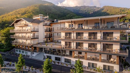 Cristallo Sport & Wellness Hotel © Andrea Acler Moderner Hotelkomplex vor bewaldeten Bergen bei Sonnenuntergang