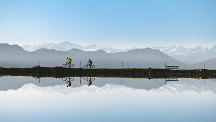 SAUKASER - PENGELSTEIN © TVB Kitzbüheler Alpen Brixental - Mathäus Gartner Two cyclists riding by a lake with mountain reflection and clear blue sky